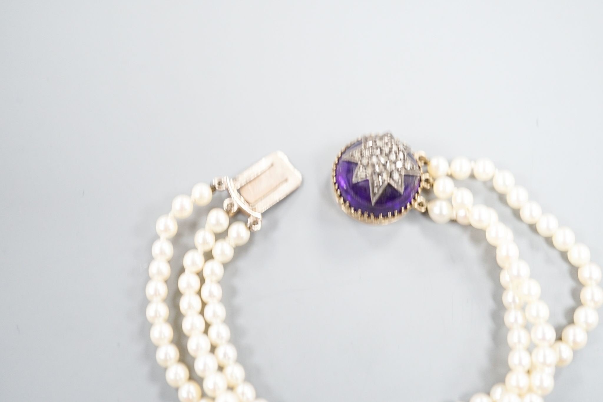 An early 20th century triple strand cultured? pearl bracelet, with rose cut diamond and cabochon amethyst set yellow metal clasp, 17.5cm, gross weight 21 grams.